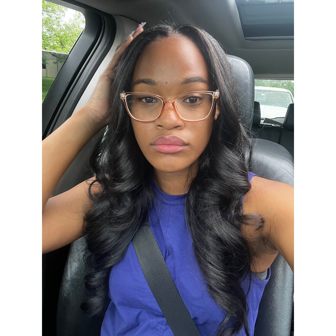 Woman sitting in a car wearing glasses and a blue shirt. wearing raw loose wave elite glam society bundles